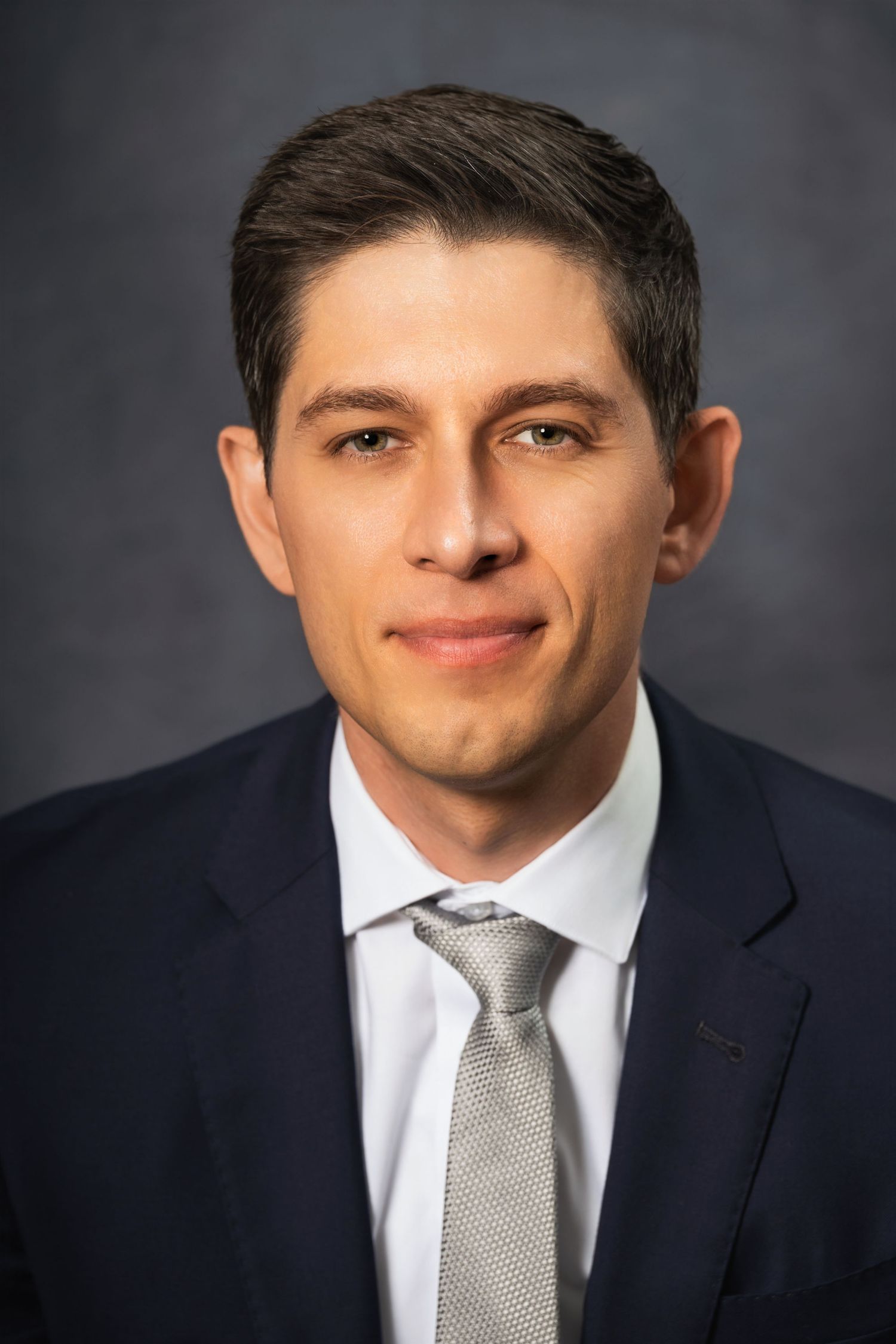 Professional studio headshot featuring a man in business attire with a neutral expression.
