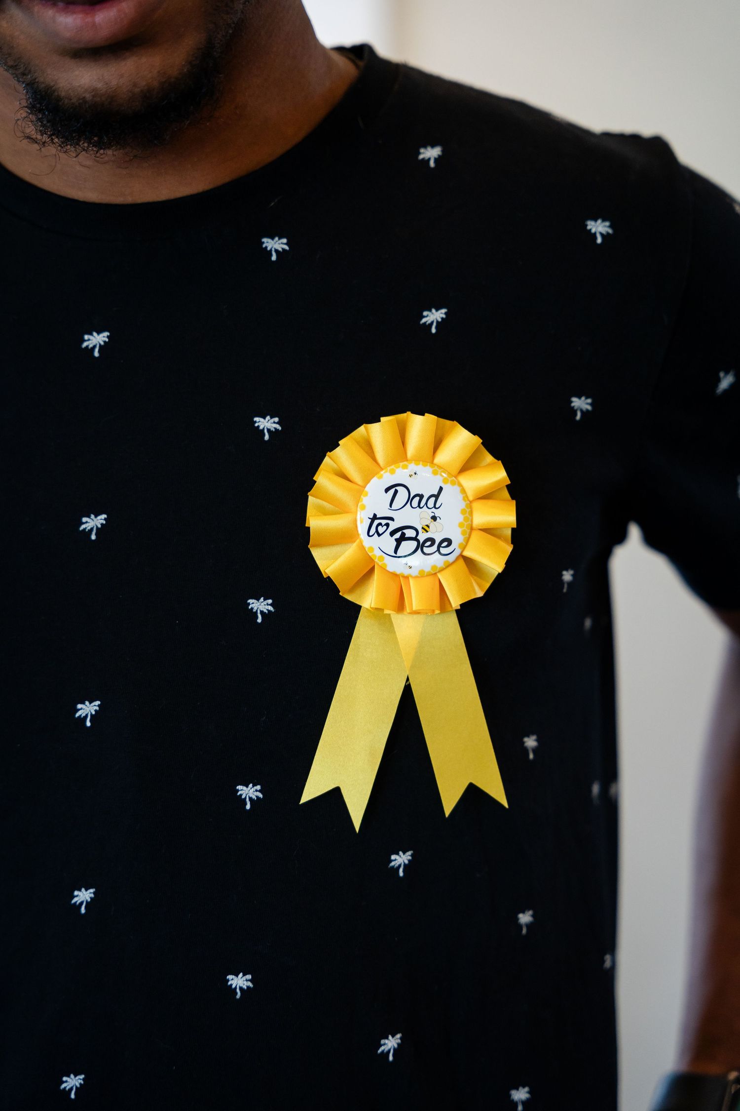 A yellow 'Dad to Bee' ribbon pinned on a black shirt with bee pattern details.