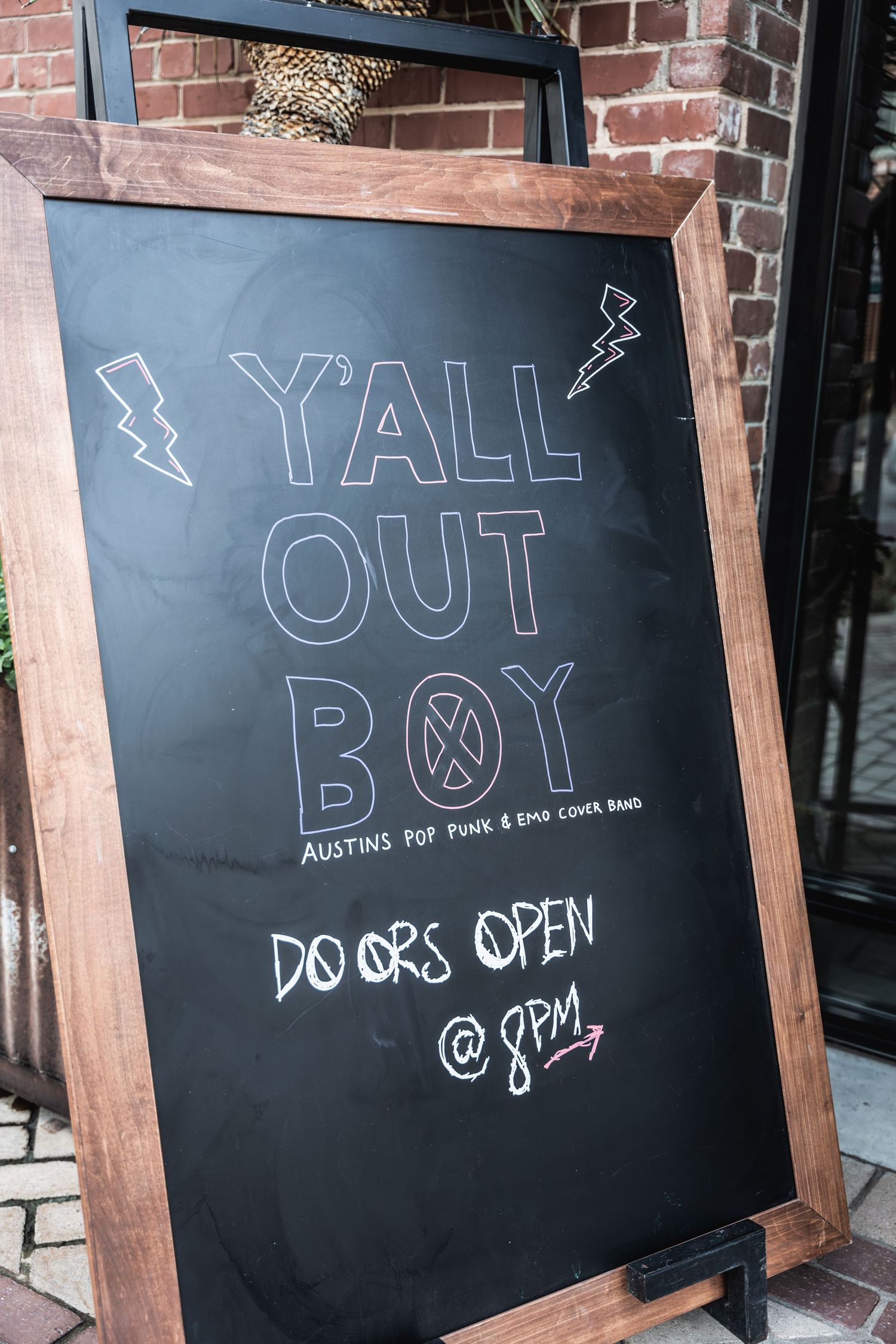 Chalkboard sign with lightning bolt designs announcing 'Yall Out Boy' performance with doors opening at 8pm.