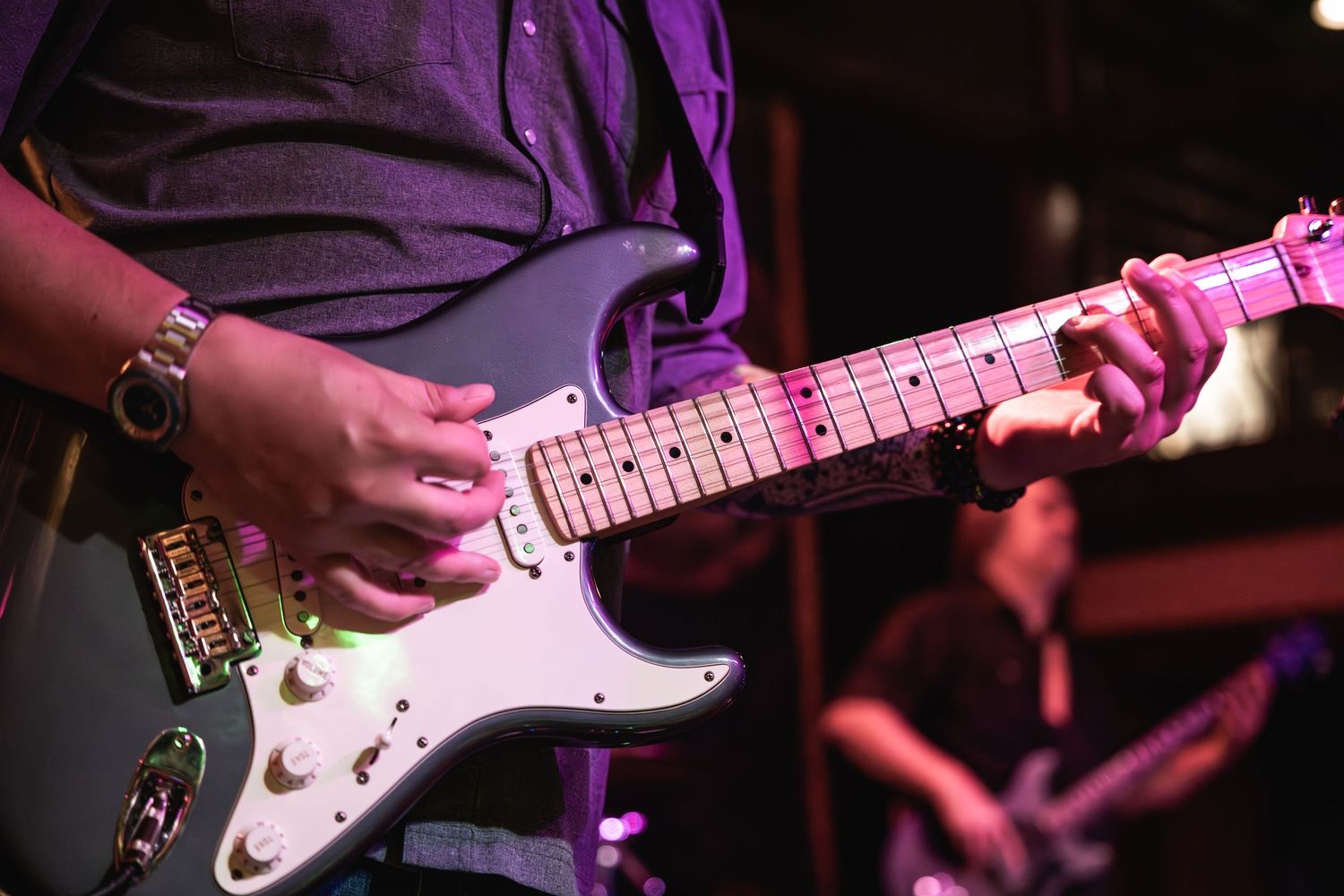 Close-up of hands playing white electric guitar on dimly lit stage.