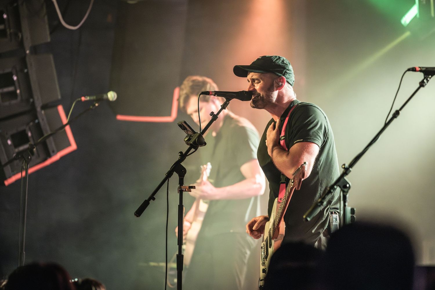 Musicians performing on stage with dramatic green and white spotlights during a live show.