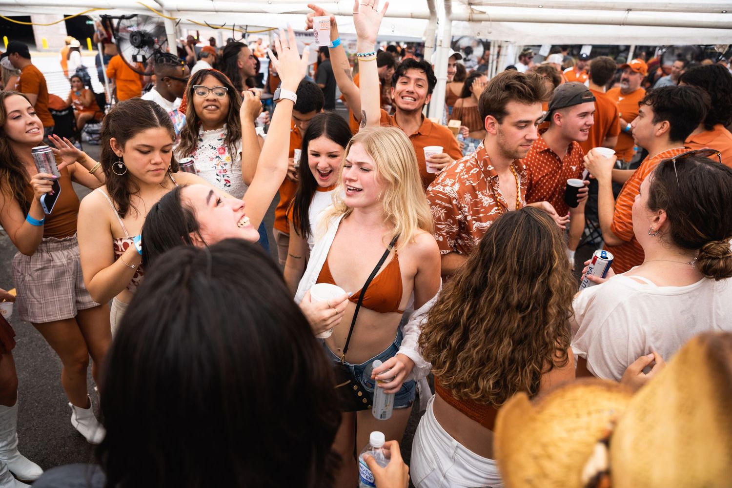 Crowd in orange and white attire celebrating enthusiastically at an outdoor party.