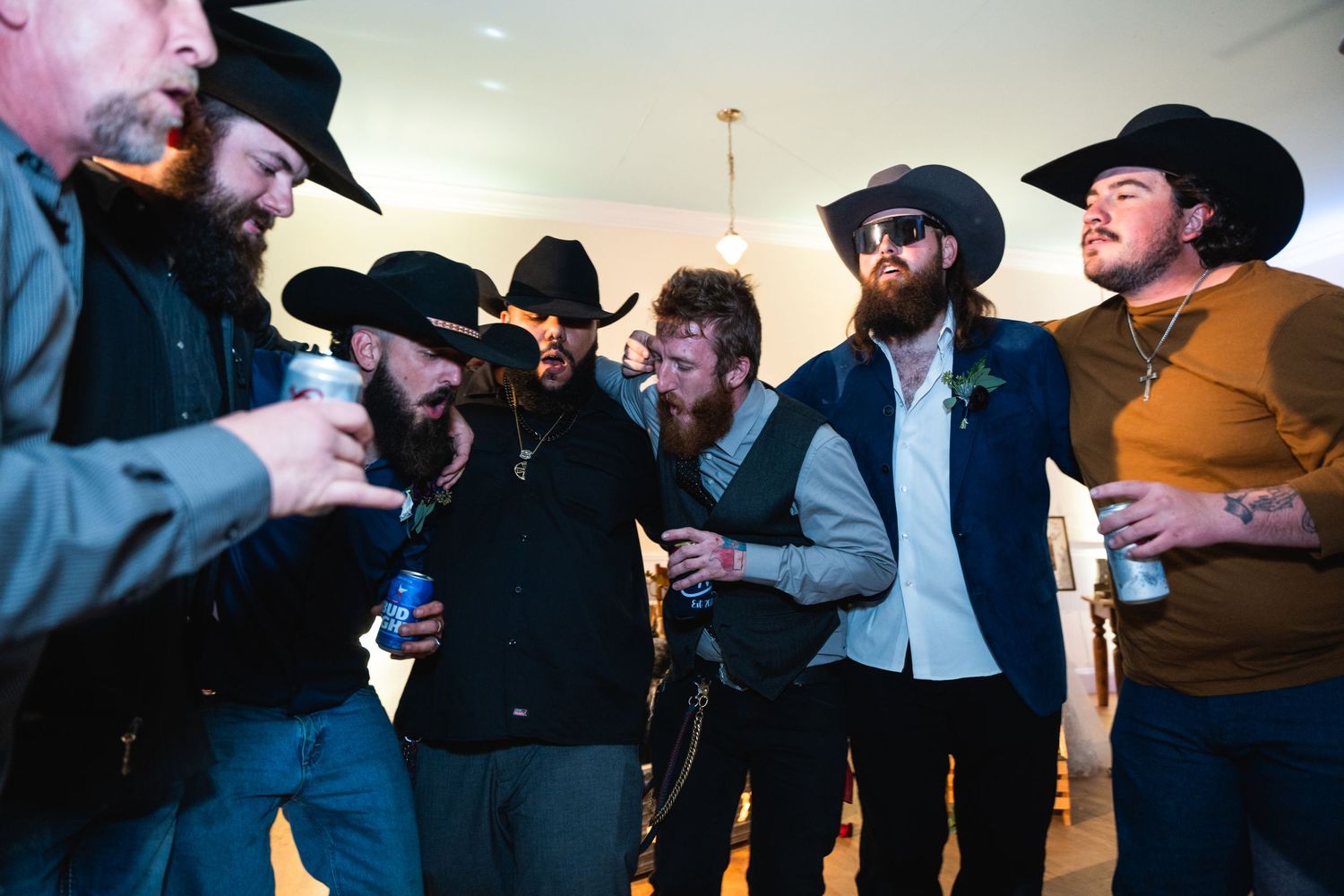 Group of friends in western attire sharing drinks and laughs at an indoor gathering.