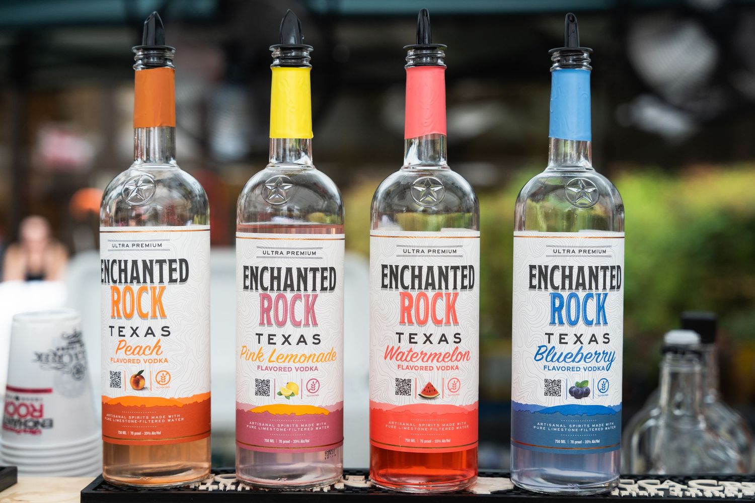 Four colorful bottles of Enchanted Rock flavored vodka lined up on display.