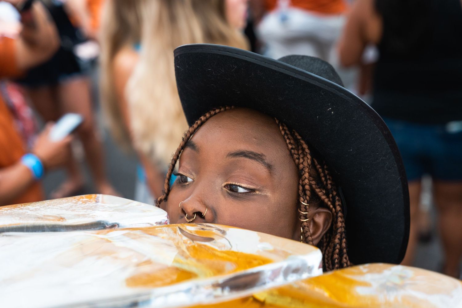 Person in black hat drinking from an ice luge at an outdoor party.