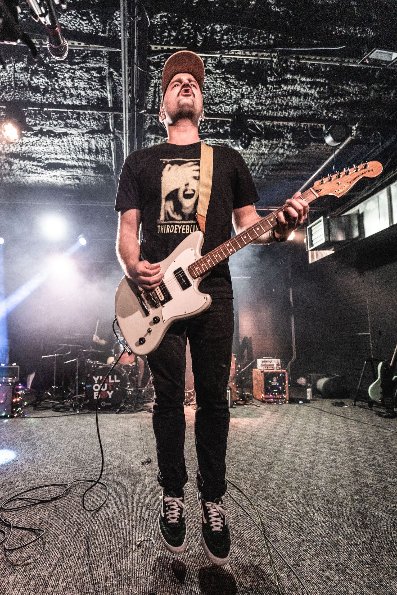 Musician playing white electric guitar while jumping during concert performance.