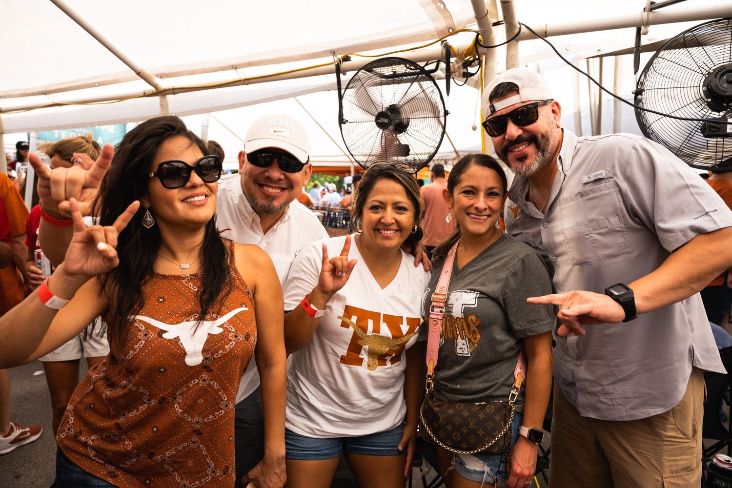 Group of Texas Longhorns fans pose together under a tent at a tailgate celebration.