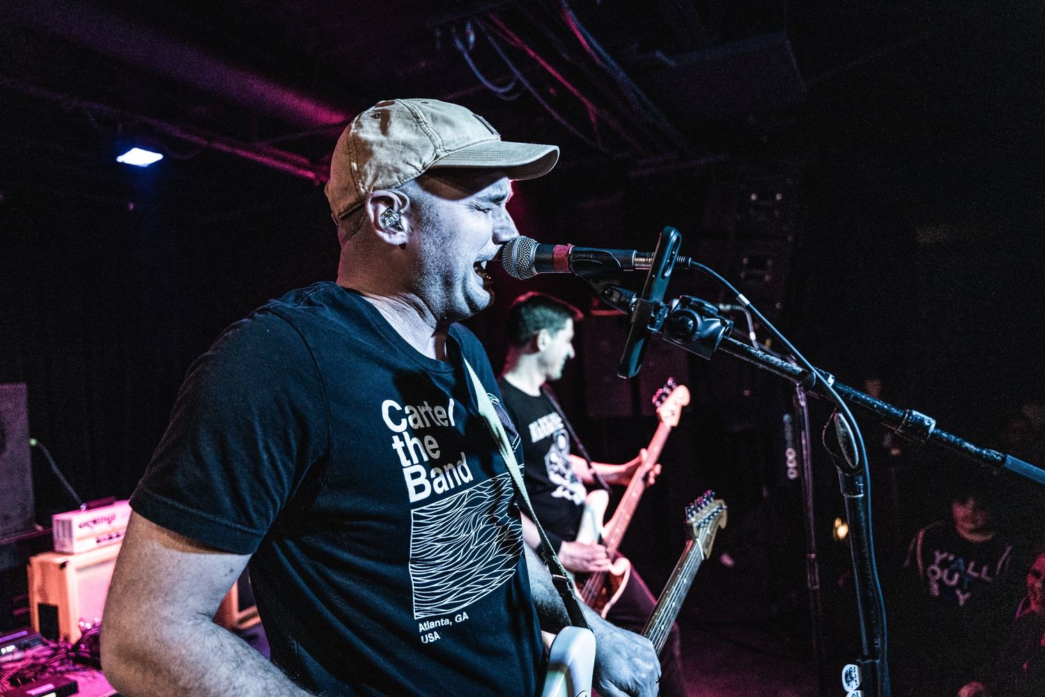 Musician singing into microphone while playing guitar at live concert venue.