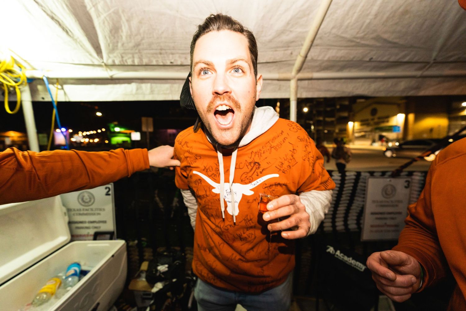 Excited person in orange hoodie gesturing enthusiastically in dimly lit indoor setting.