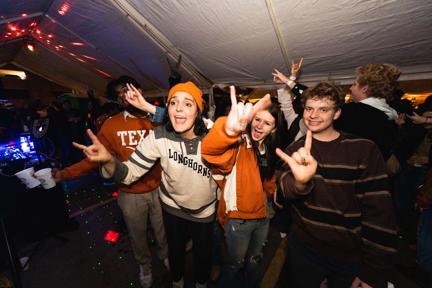 Party crowd enjoying themselves with arms raised under colorful lighting at a night event.