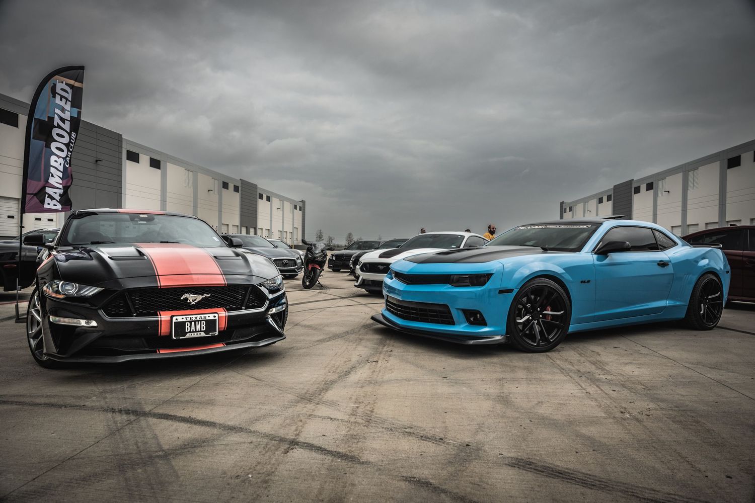 Black striped Mustang and blue Camaro facing each other in dramatic automotive photoshoot.