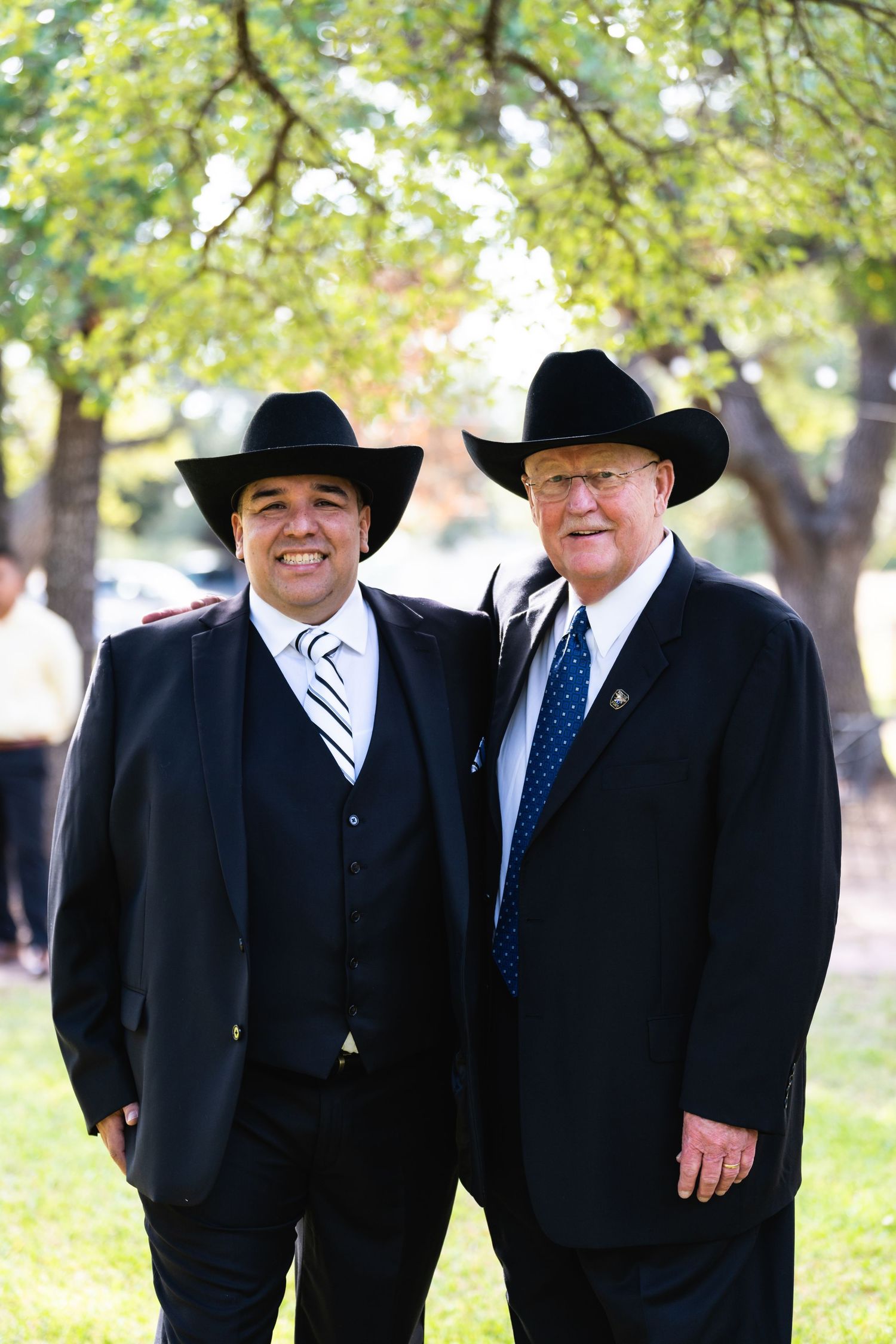 Two men in black suits and cowboy hats stand together outdoors at a formal event.