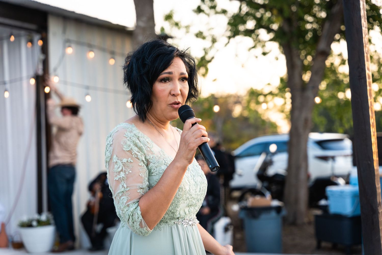Person in a mint green dress speaking into a microphone at an outdoor event during sunset.