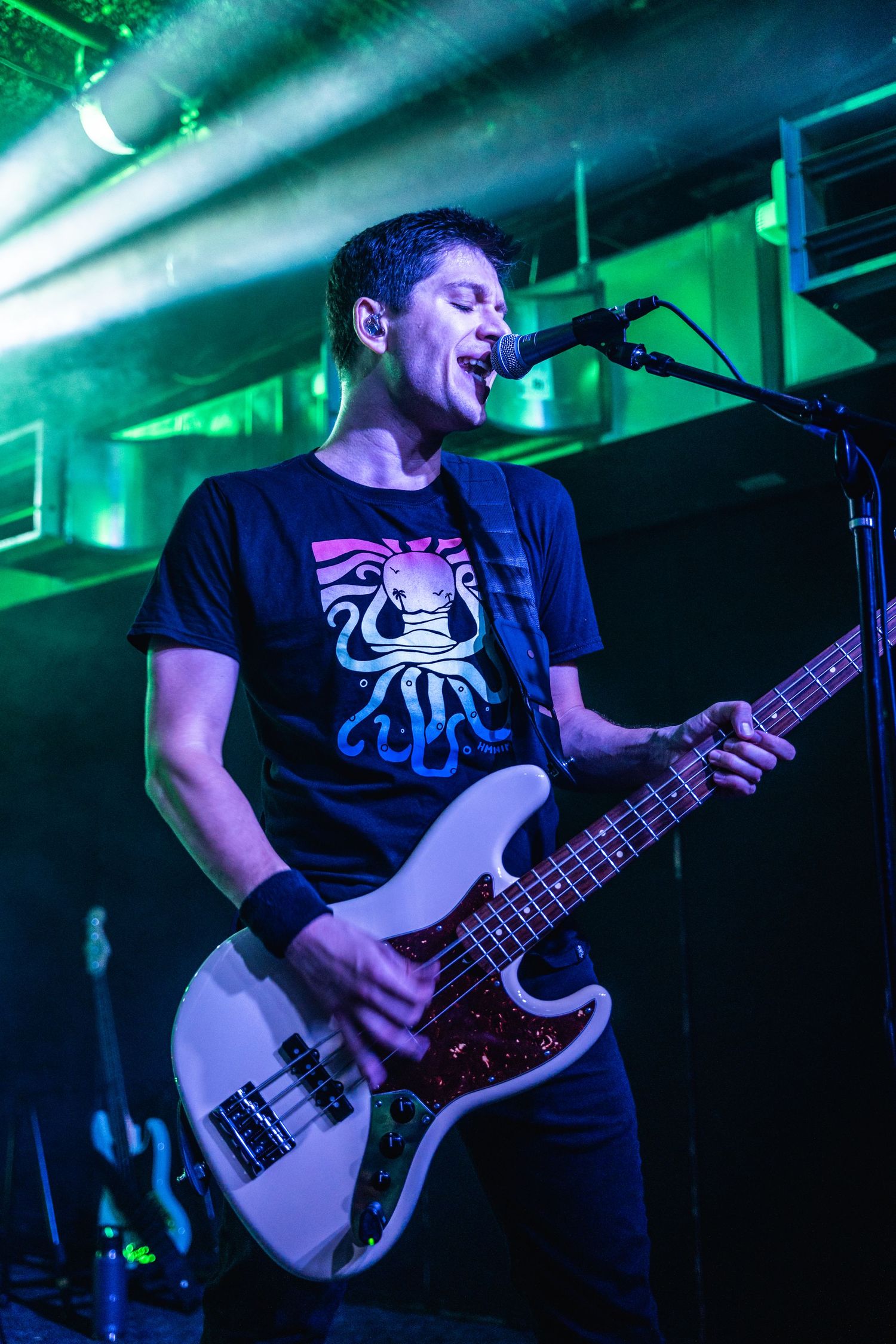 Bass guitarist performs on stage under dramatic green and blue lighting effects.