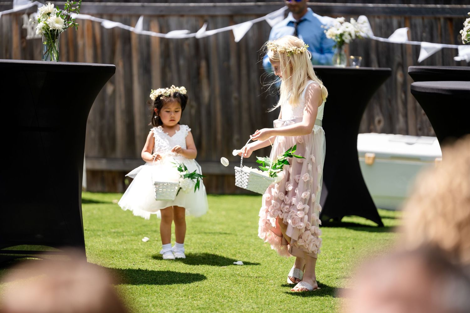 Two attendants in white and pink dresses walk across grass at outdoor wedding.