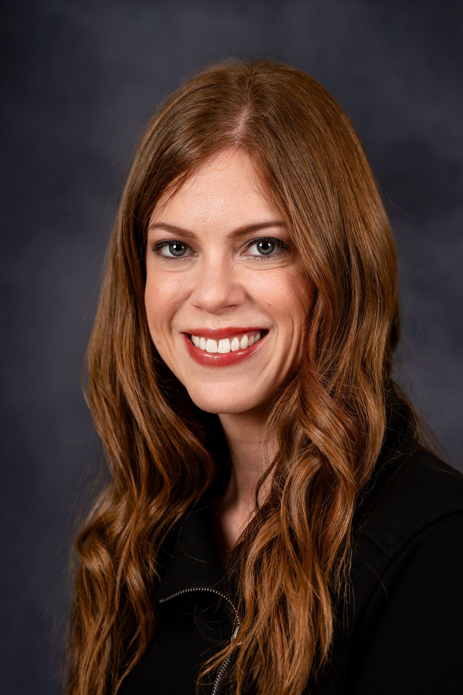 Studio portrait with long wavy brown hair and black top against dark background.