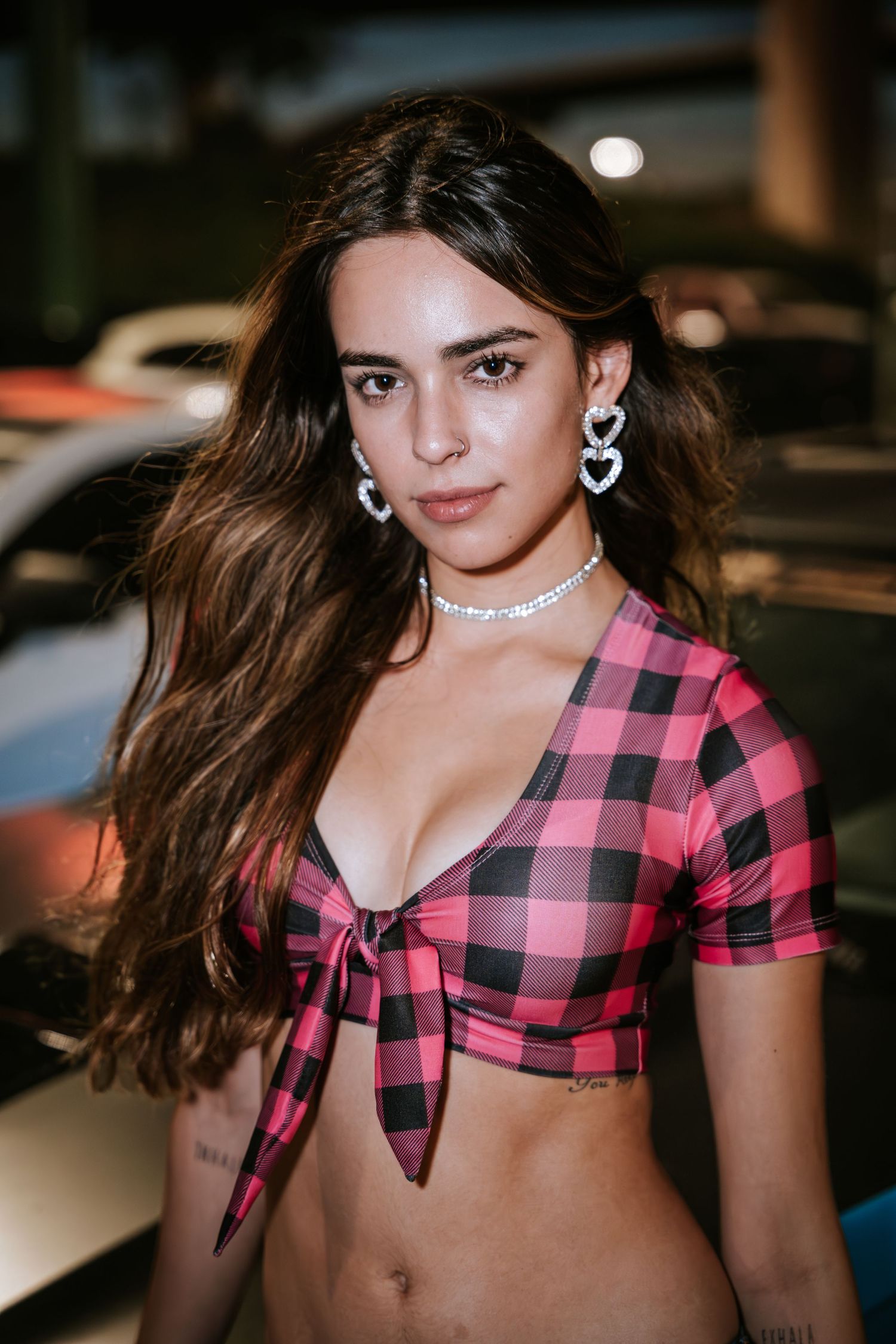 Model wearing pink buffalo check tied top and silver necklace poses outdoors.