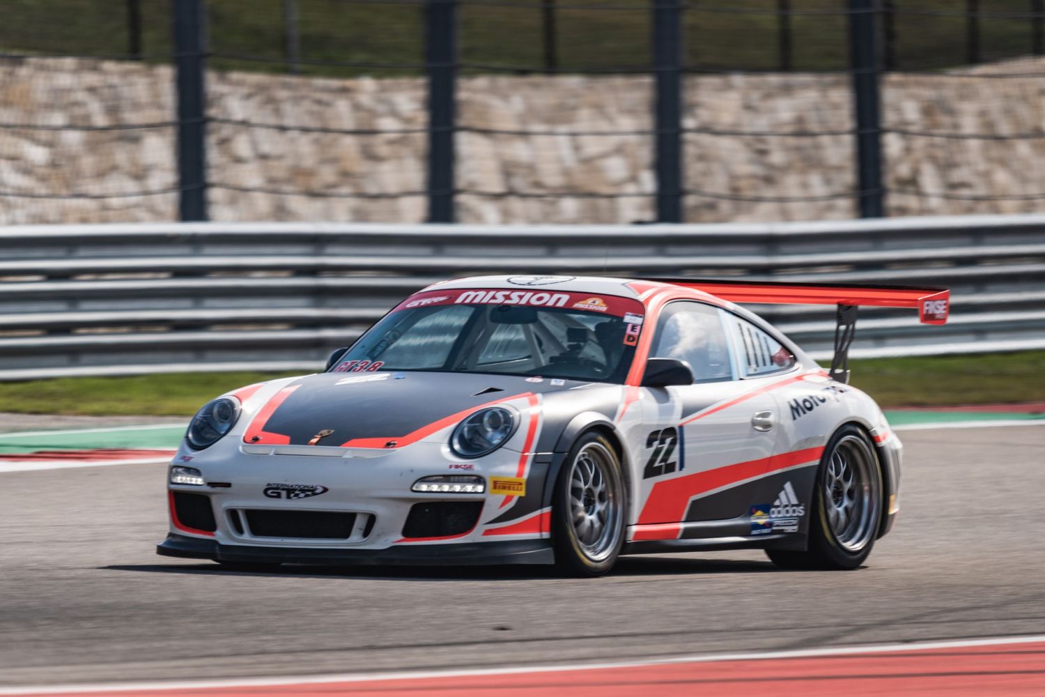 White Porsche GT3 Cup car races on a professional motorsport track.