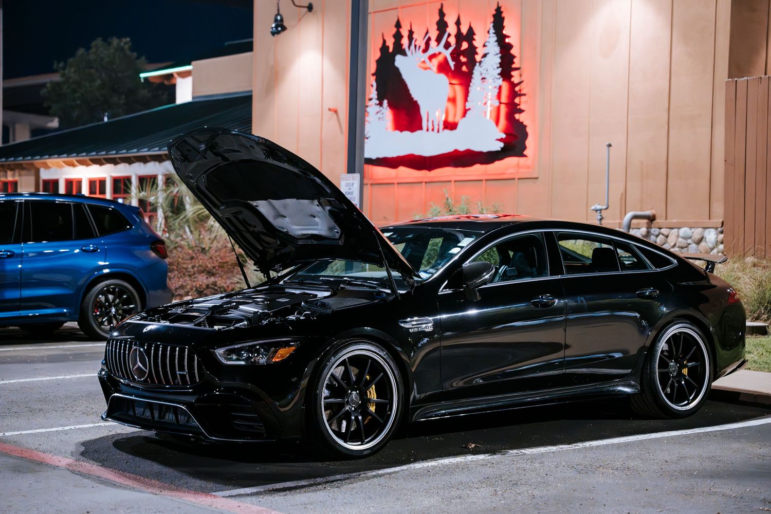 Black Mercedes-AMG GT sedan with open hood displayed at night car meet.