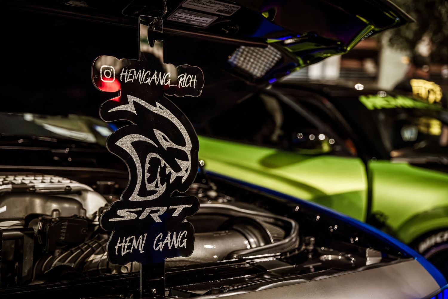 Close up of black Hellcat engine with SRT badge under hood lighting.