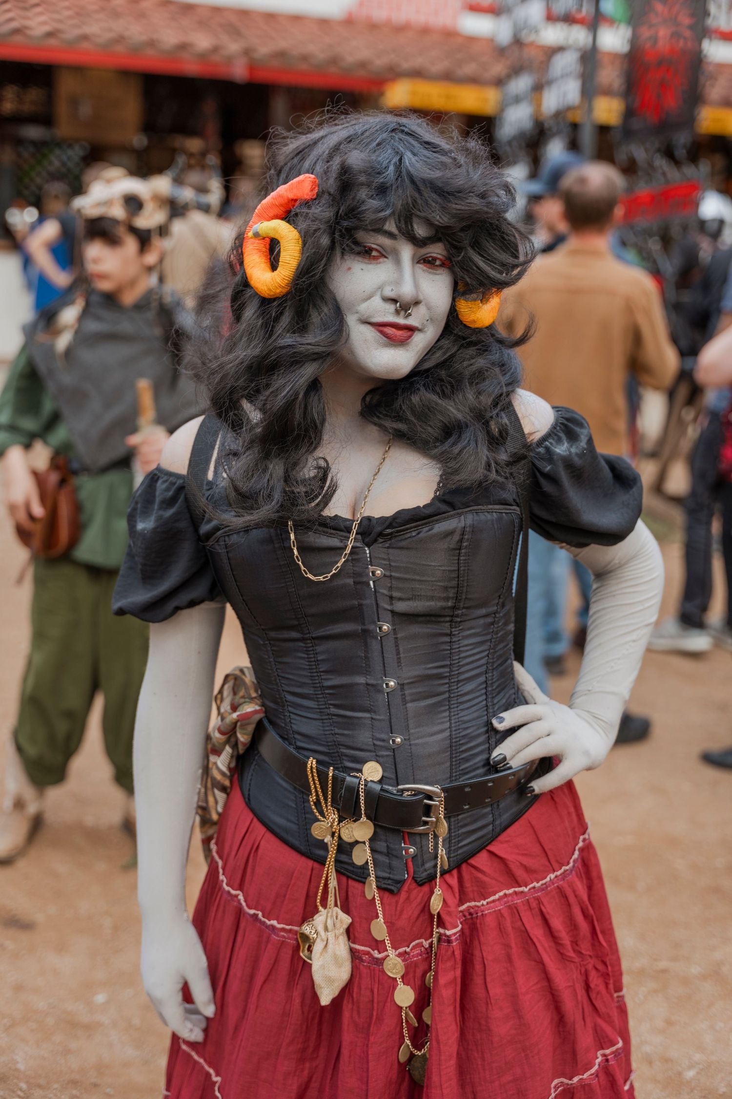 A costumed performer in a black corset and red skirt with orange earmuffs at a renaissance festival.