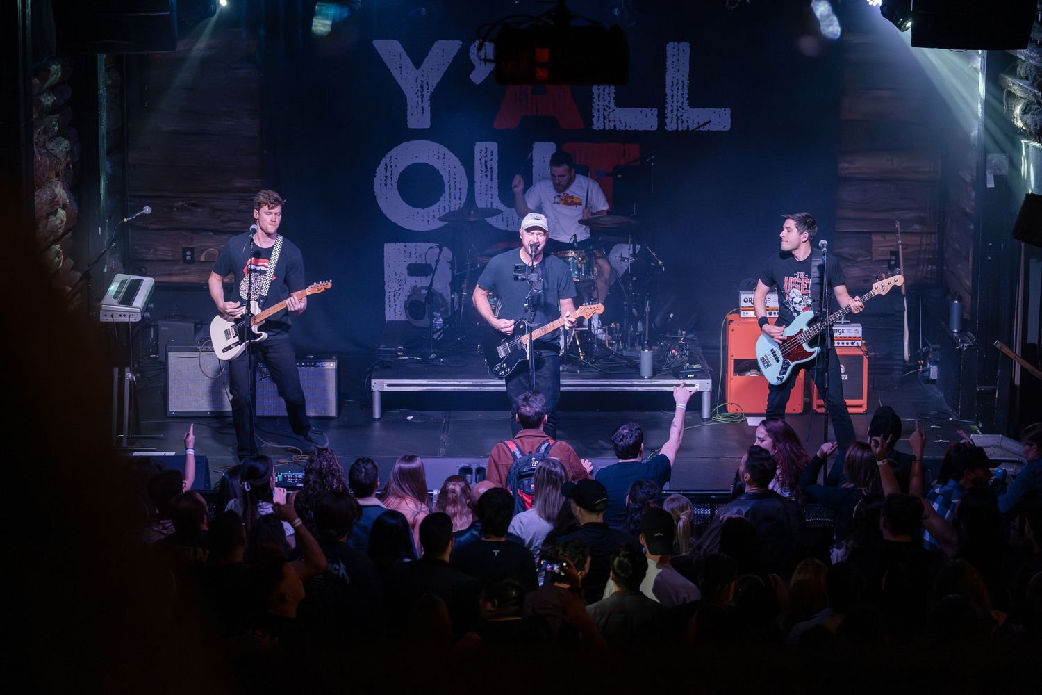 Band members perform on stage under dramatic lighting with 'YO' text visible in the background.