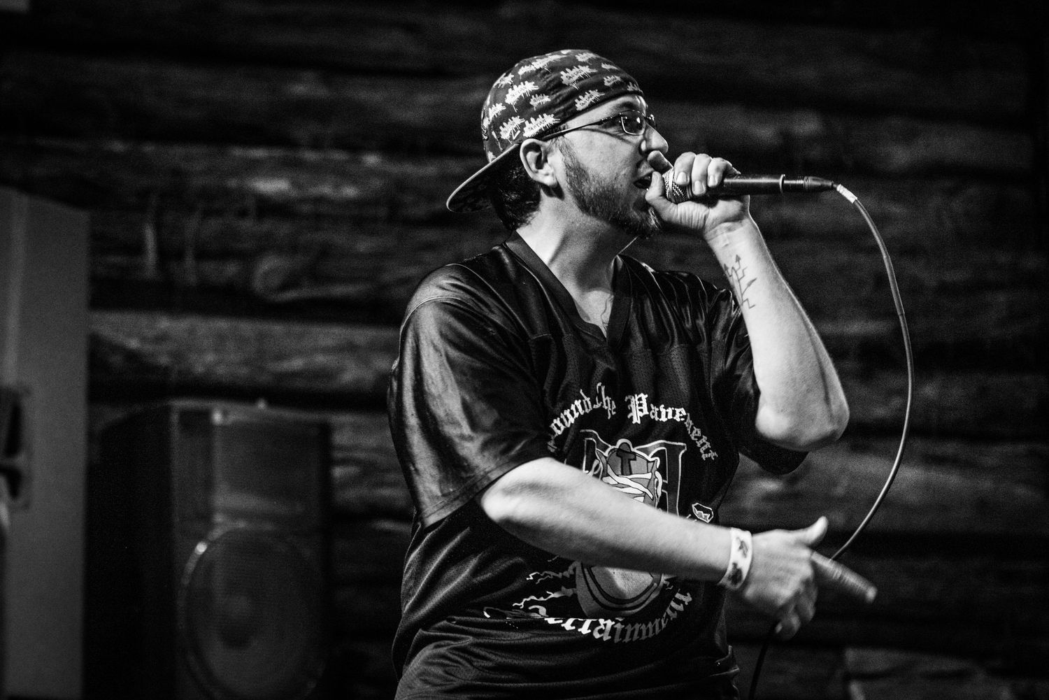 Black and white photo of performer in bandana singing into microphone during live show.