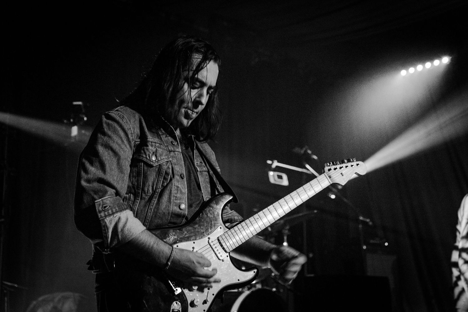 A guitarist performs on stage in dramatic lighting during a rock concert performance.