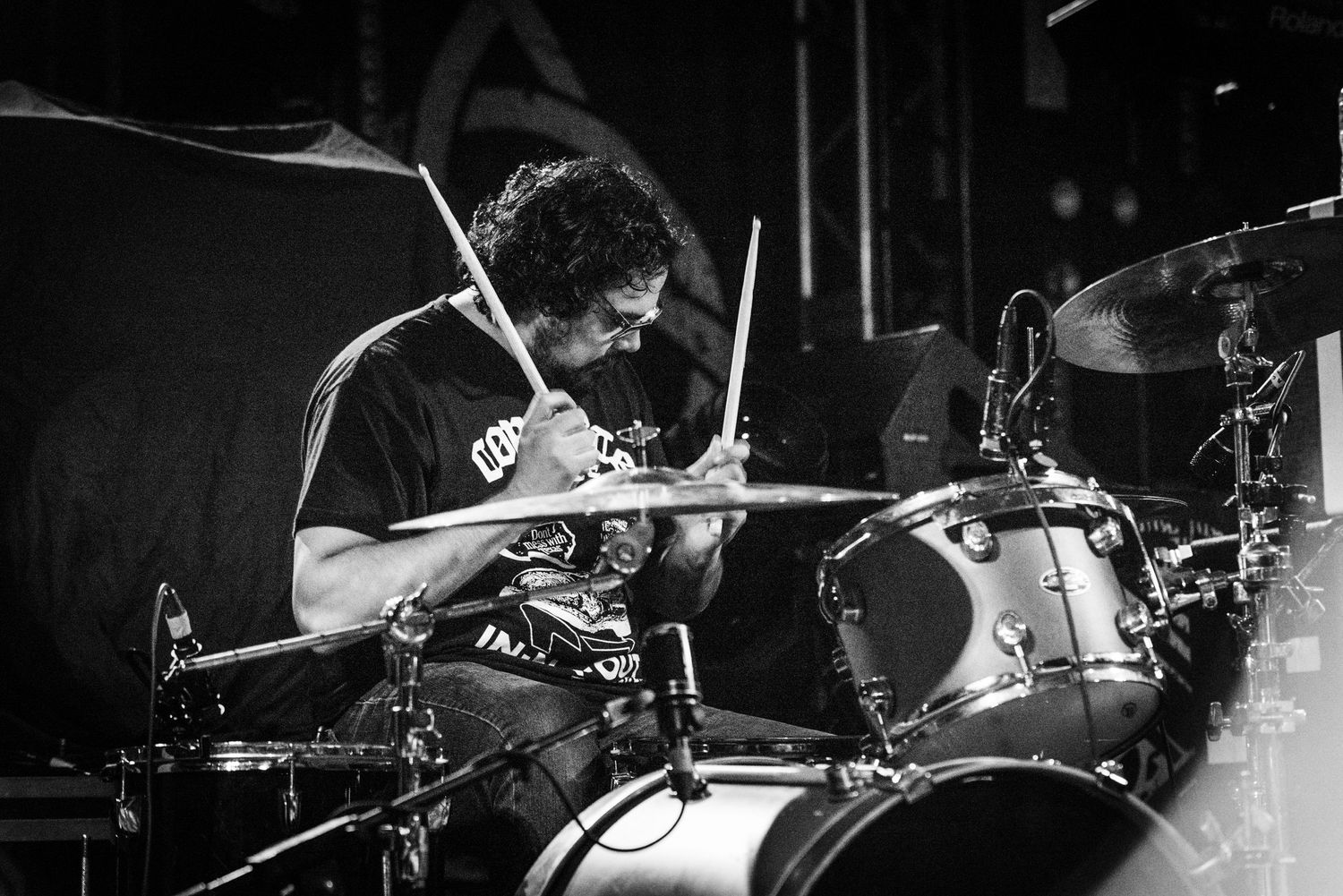 Drummer performing at a live concert in dramatic black and white lighting.