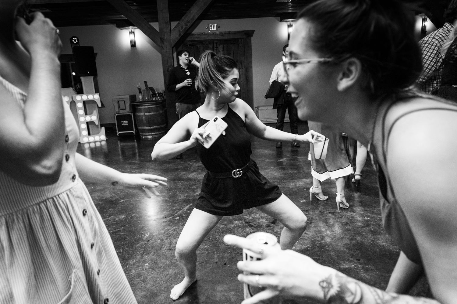 Wedding guests dance and laugh at reception in black and white photography.