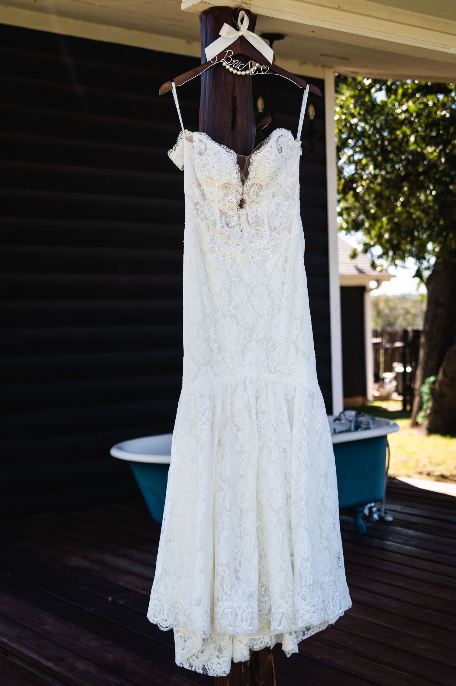Elegant white lace wedding dress with spaghetti straps hanging on display outdoors.