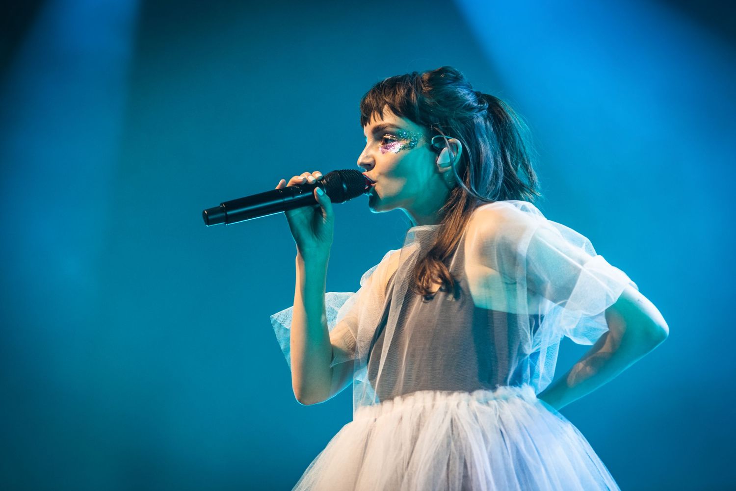 Singer performs in ethereal white dress under blue stage lighting.