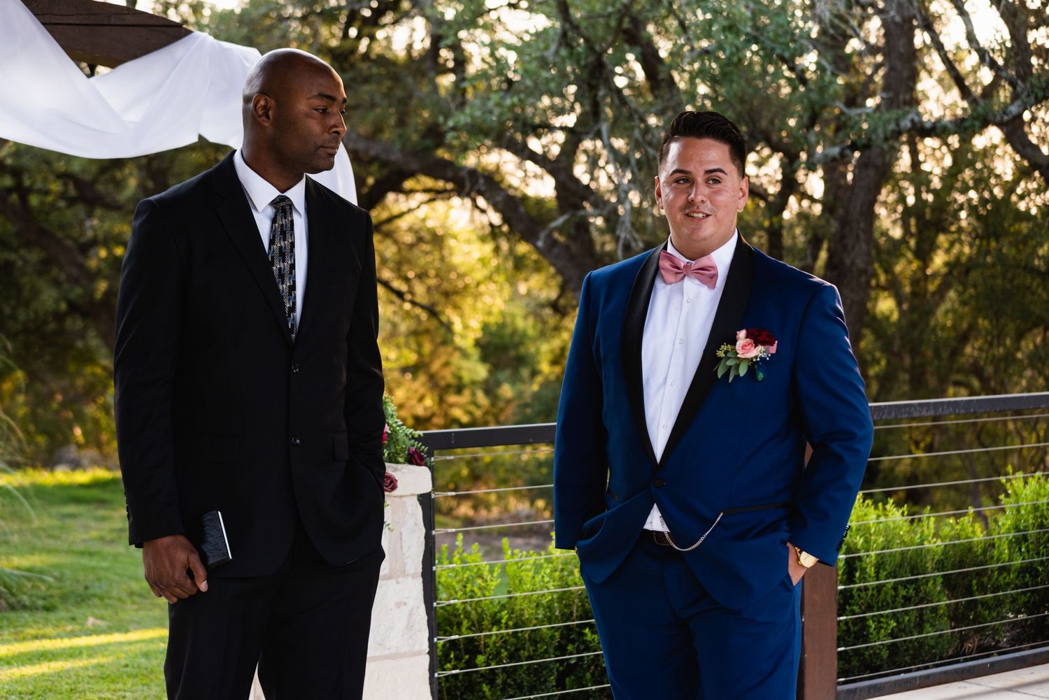 Two people in formal attire stand together at an outdoor wedding venue during golden hour.