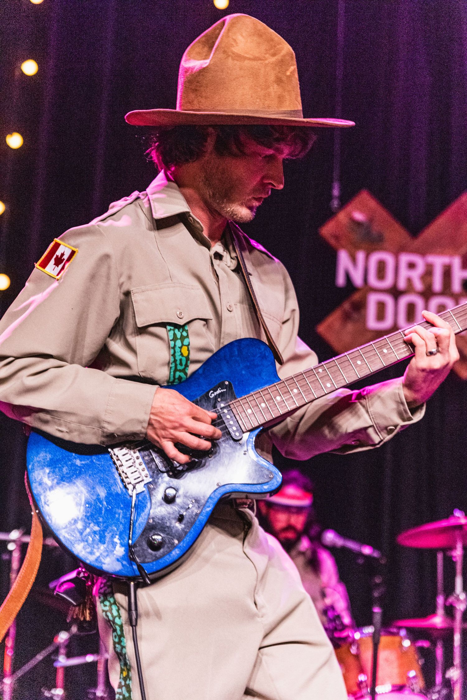 Close-up of guitarist in ranger-style uniform playing blue electric guitar during performance.