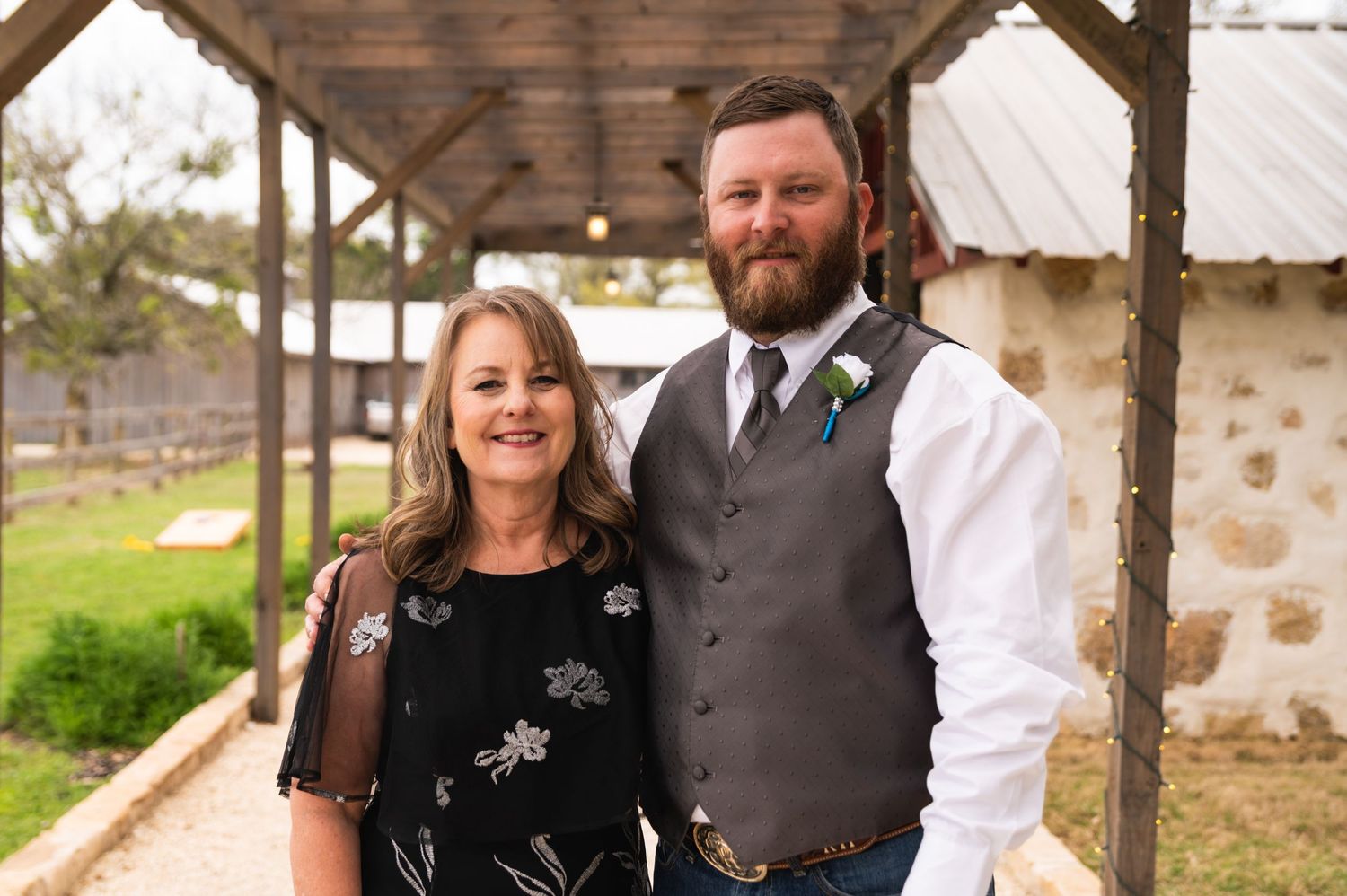 Couple in formal attire standing under wooden pavilion at rustic venue.
