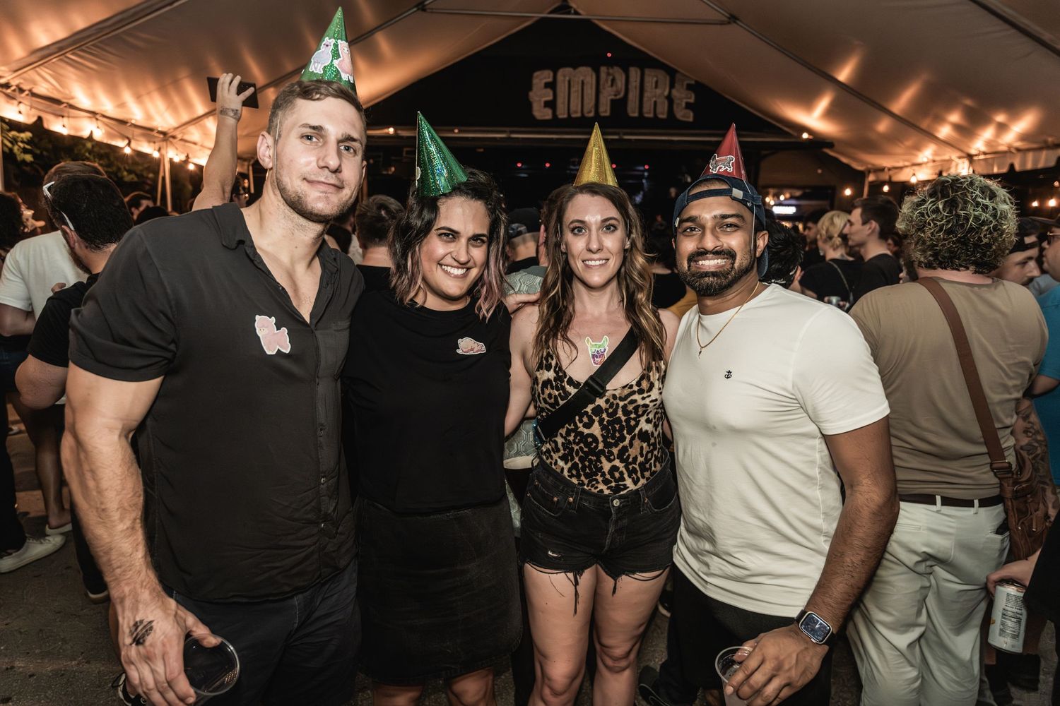 Group of friends pose together at an outdoor Empire-branded event under tent lighting.