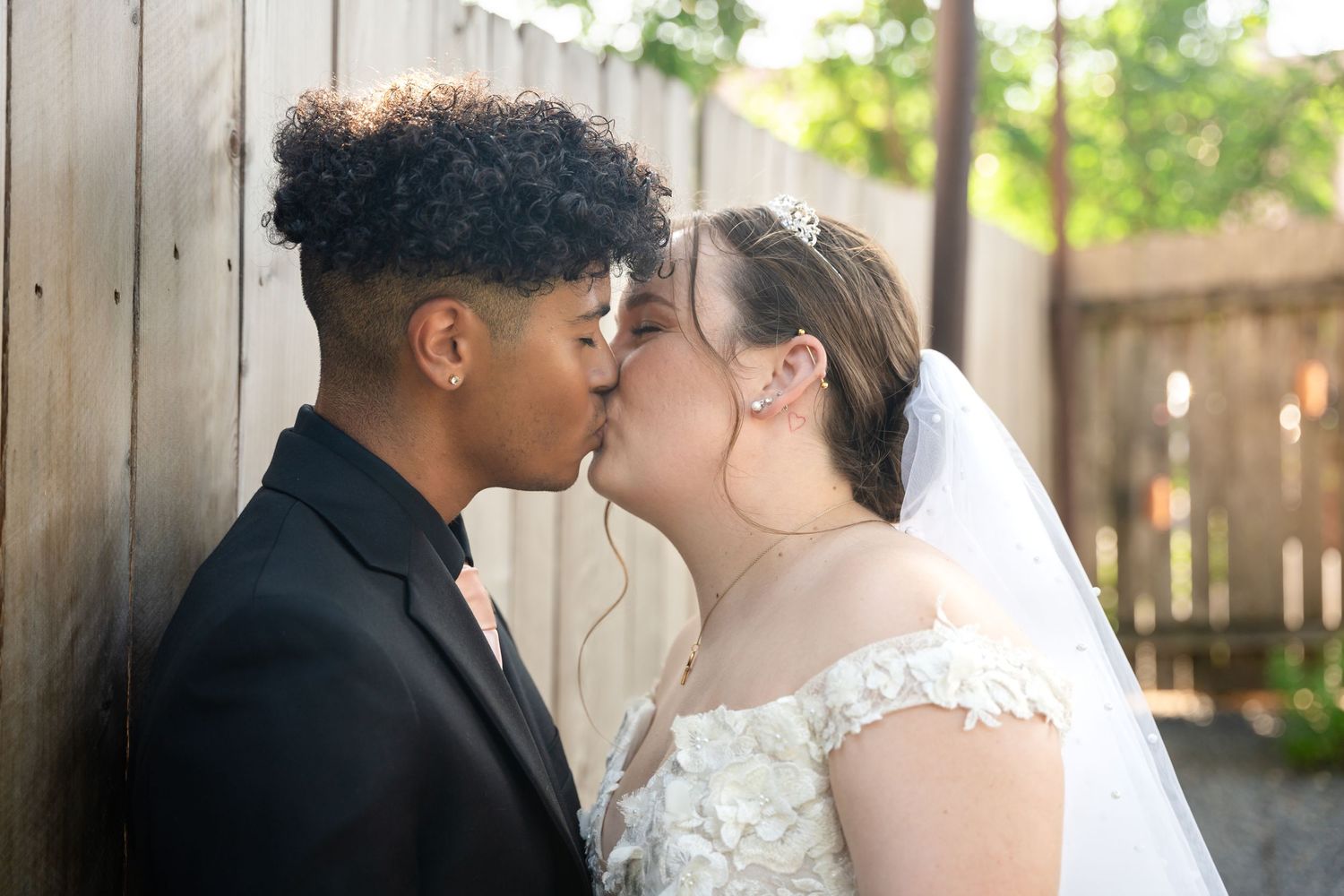 Romantic wedding moment captured against rustic wooden fence backdrop.