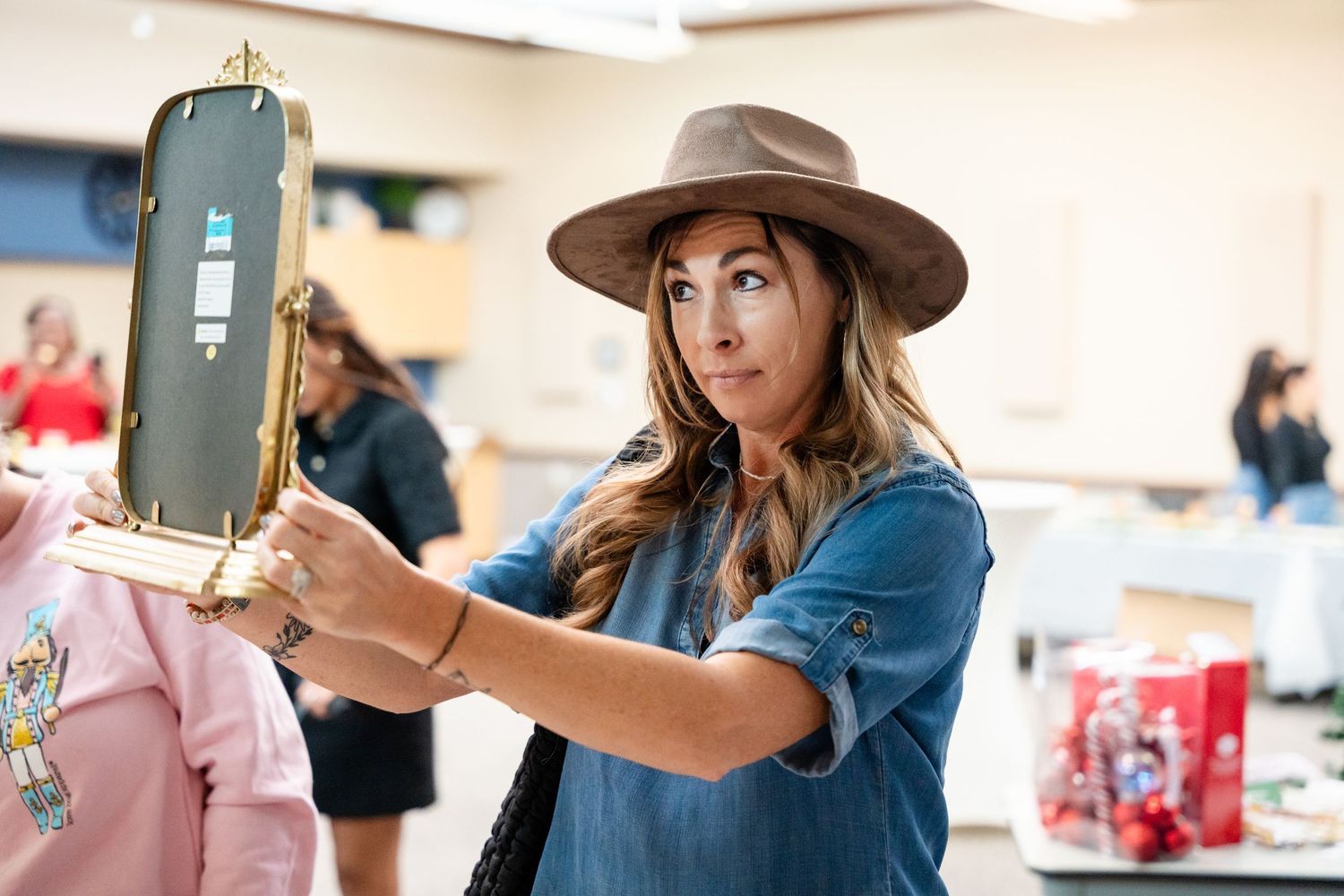 A person in denim trying on a brown fedora hat while shopping.