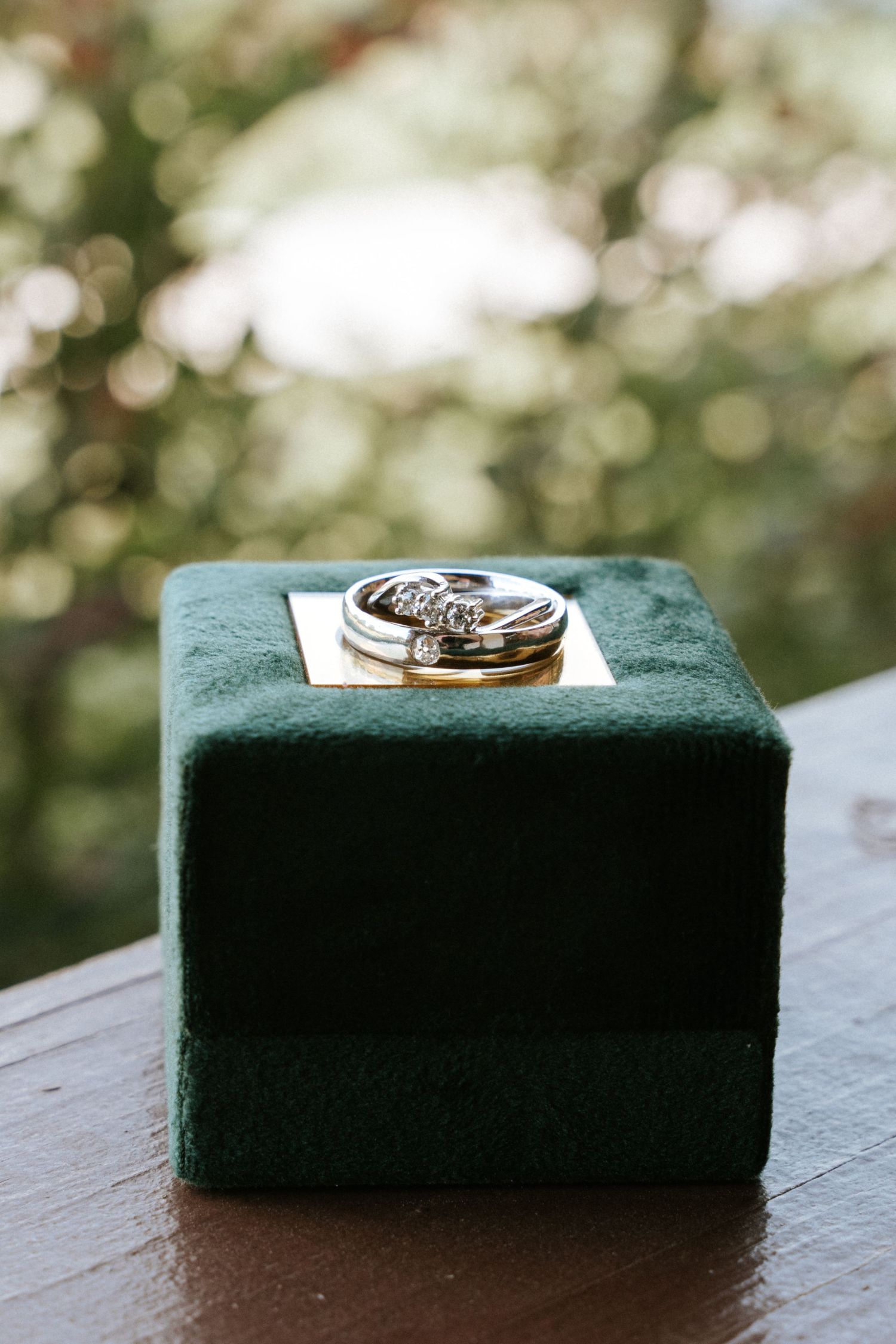 Wedding rings displayed on a dark green velvet ring box with bokeh background.