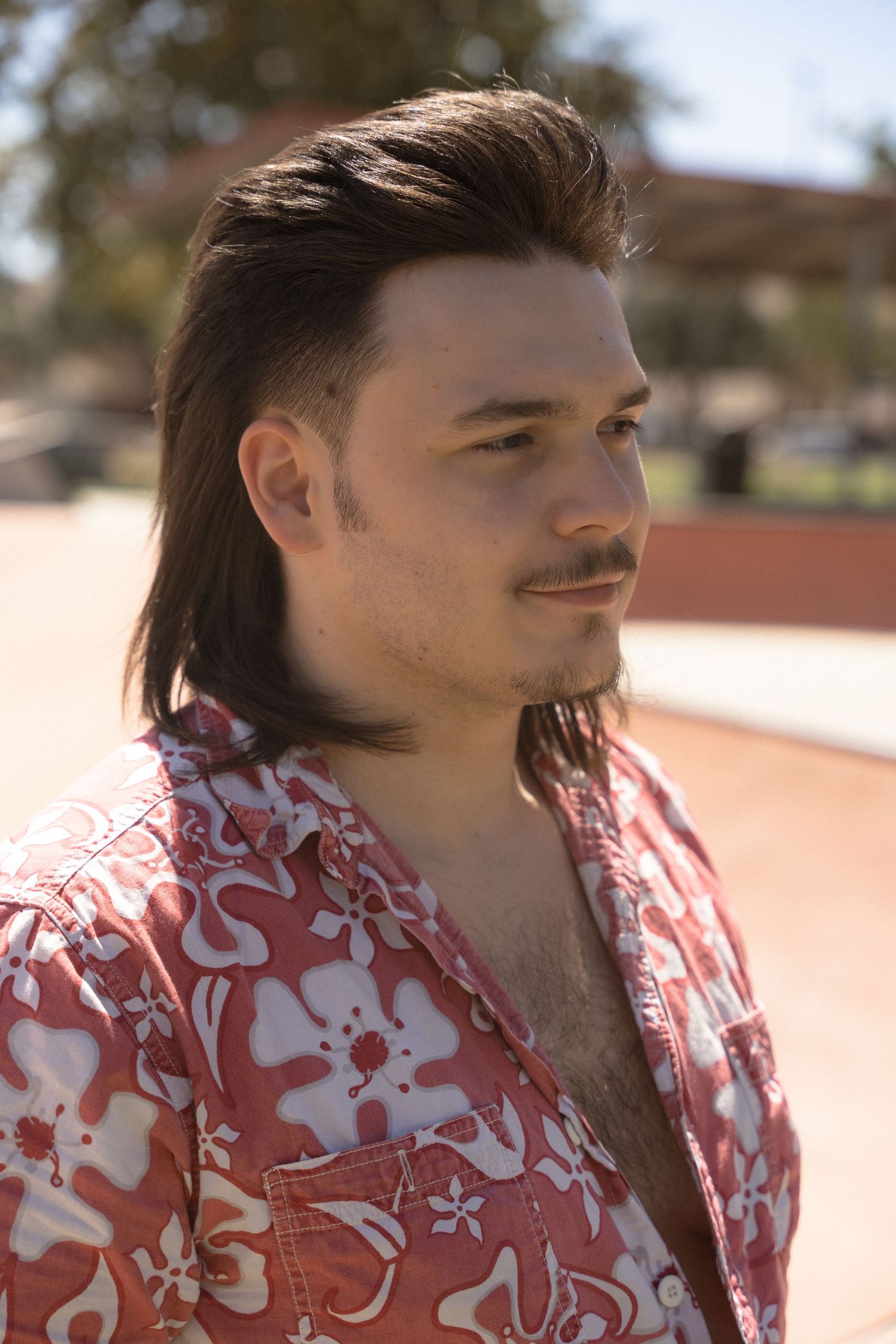 A person in a red and white floral shirt poses outdoors in natural lighting.