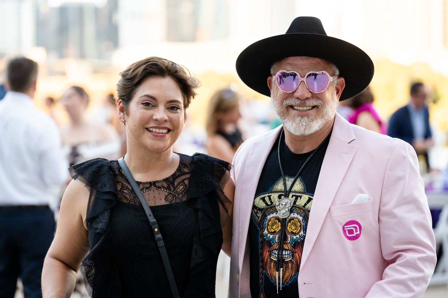 Festival attendees dressed in stylish outfits at outdoor event with city backdrop.