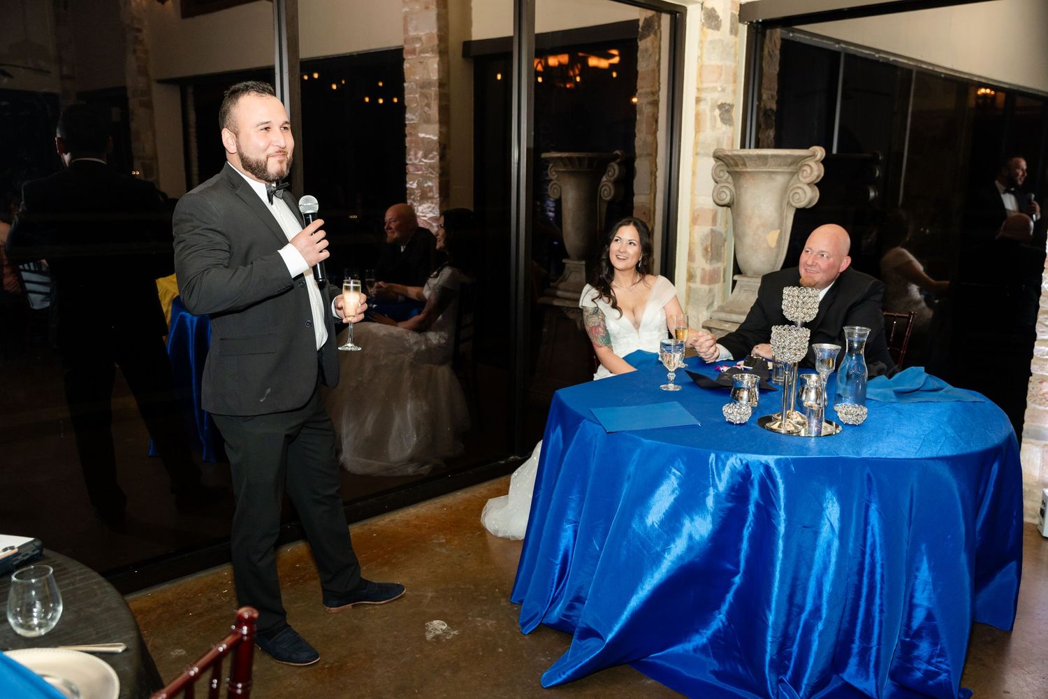 Wedding reception speech with guests seated at blue-decorated tables.