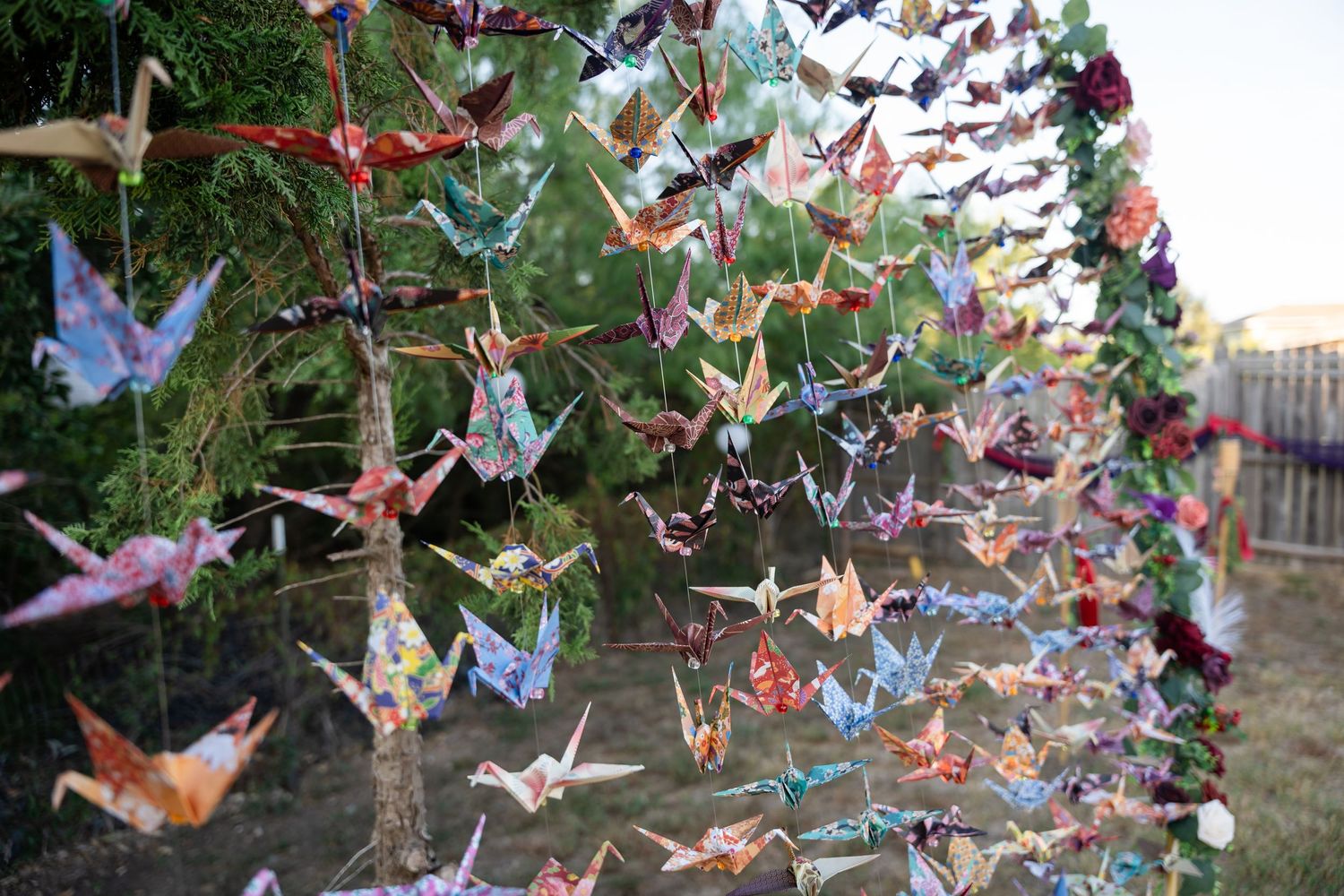 Colorful origami paper cranes hanging from strings in an outdoor setting.
