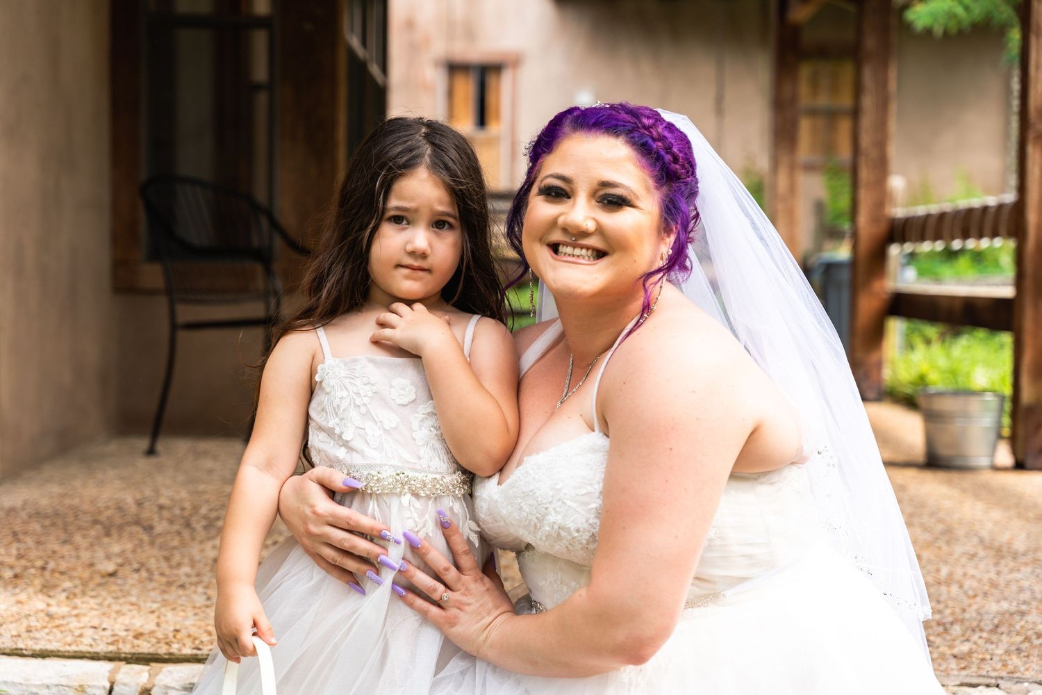 A bride in white poses with a young flower girl in a matching dress.