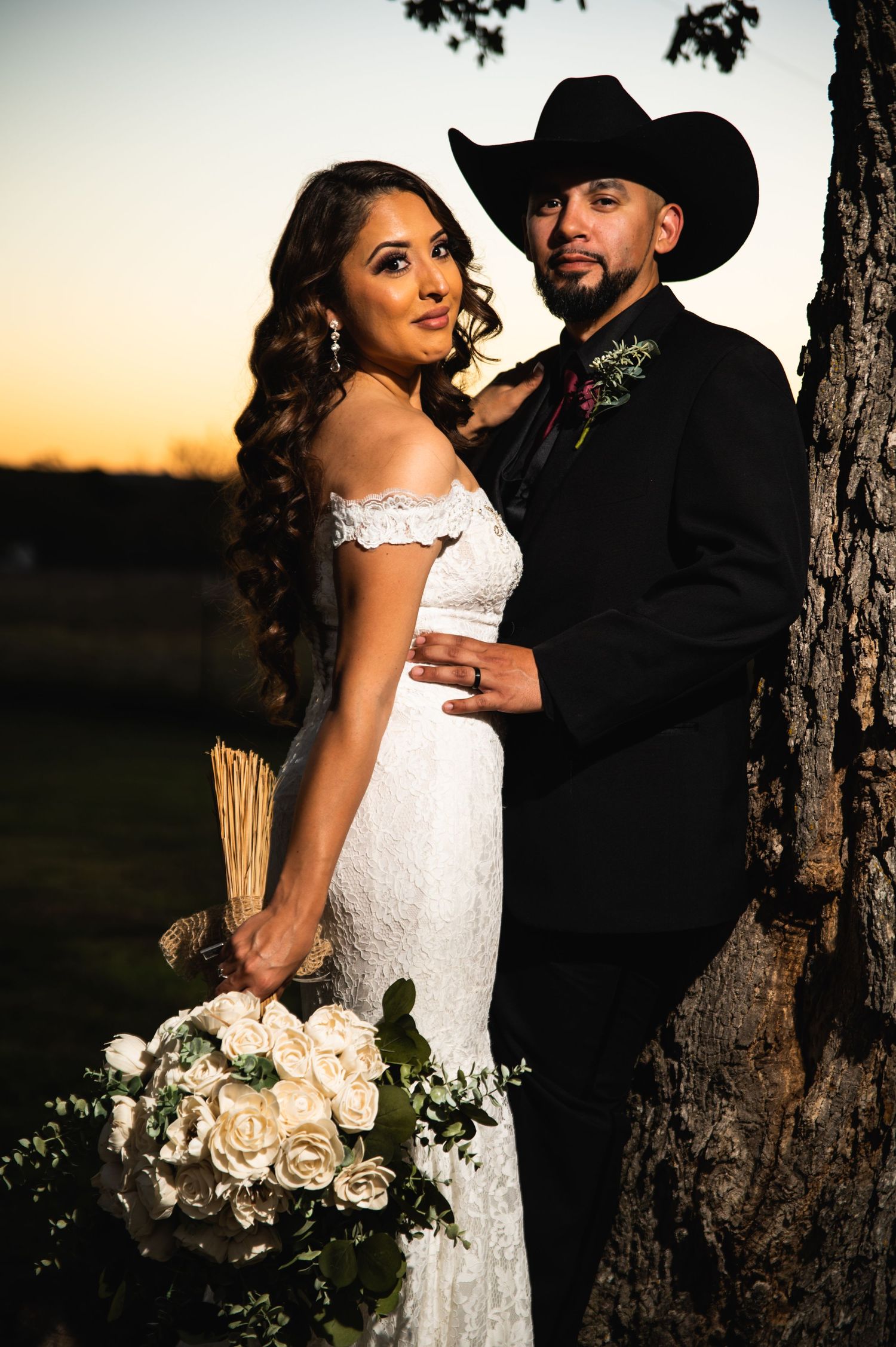 A romantic sunset portrait of a couple in wedding attire against a tree.