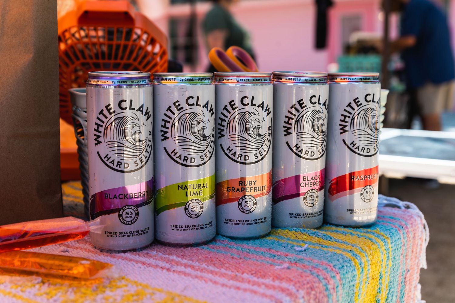 A row of White Claw hard seltzer cans displayed on a colorful rainbow tablecloth.