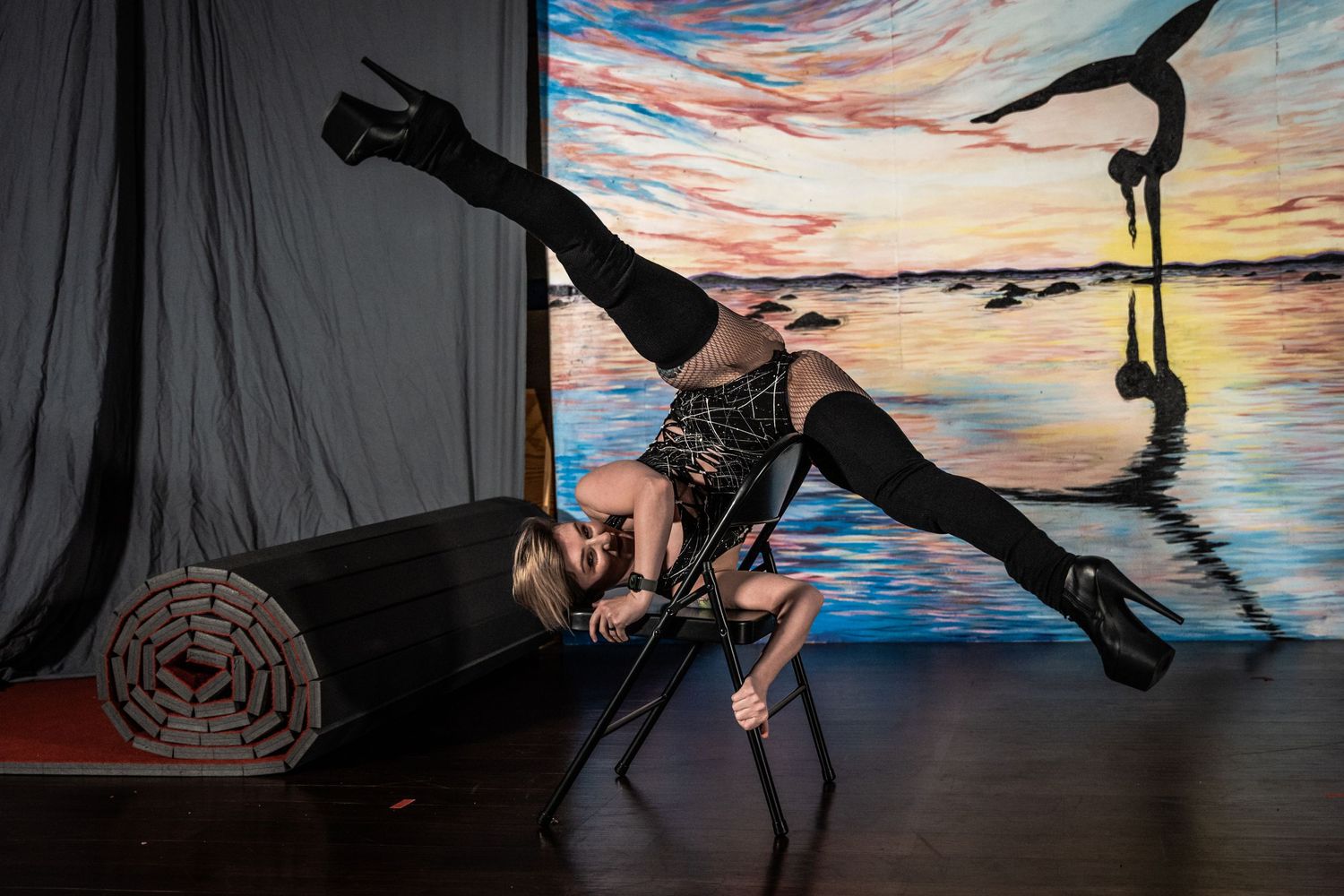 Dancer performs dramatic split pose against sunset backdrop in dance studio.