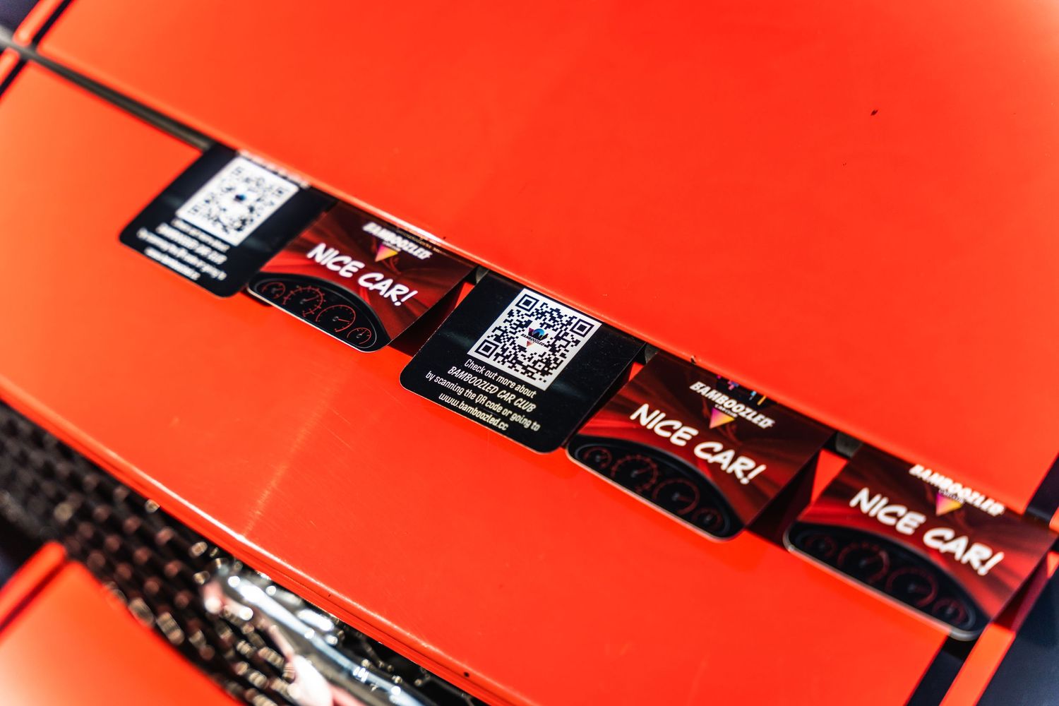 Close-up of red and black racing decals on an orange car hood.