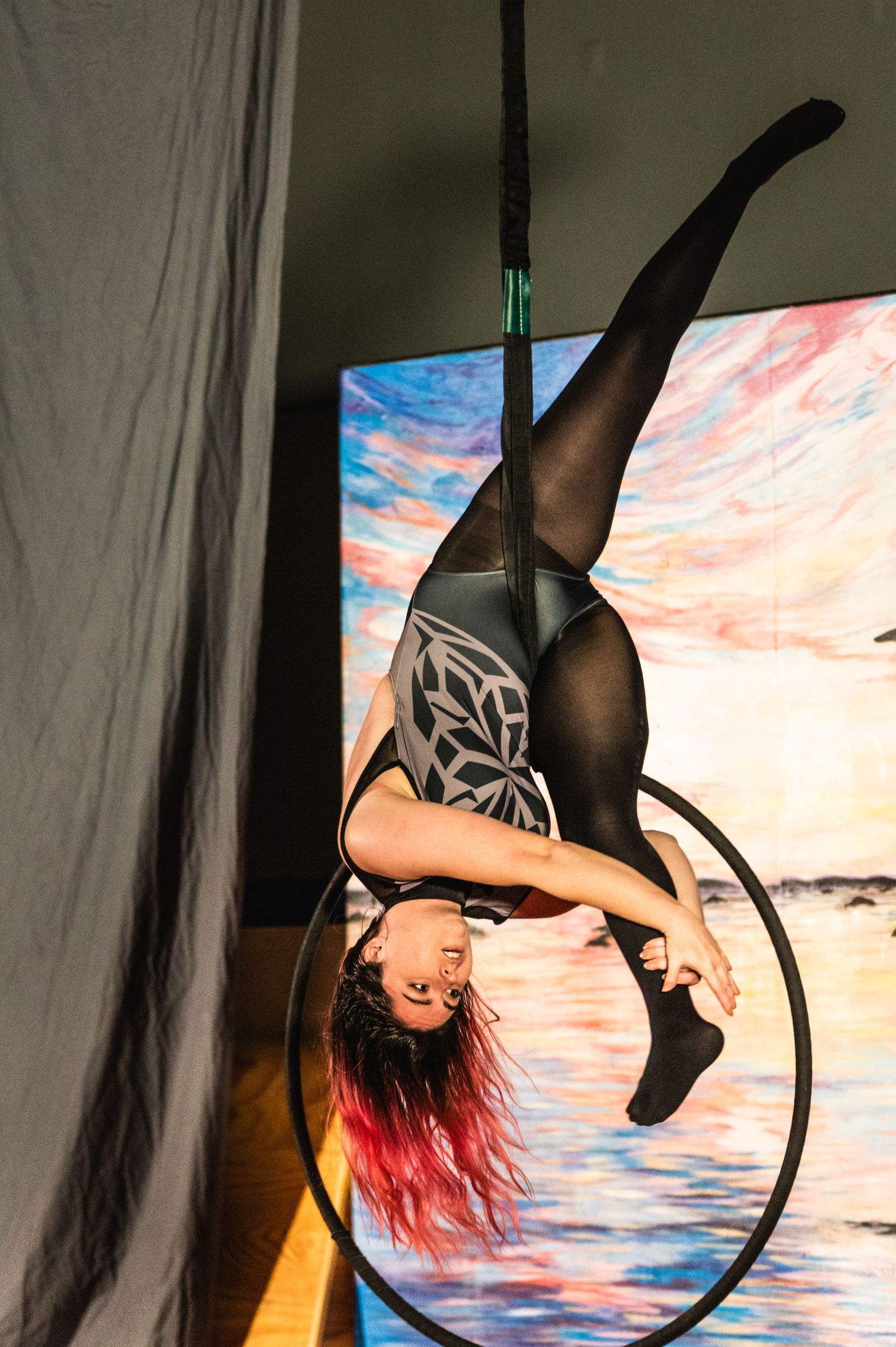Aerial performer gracefully poses on hoop against colorful backdrop in theatrical lighting.