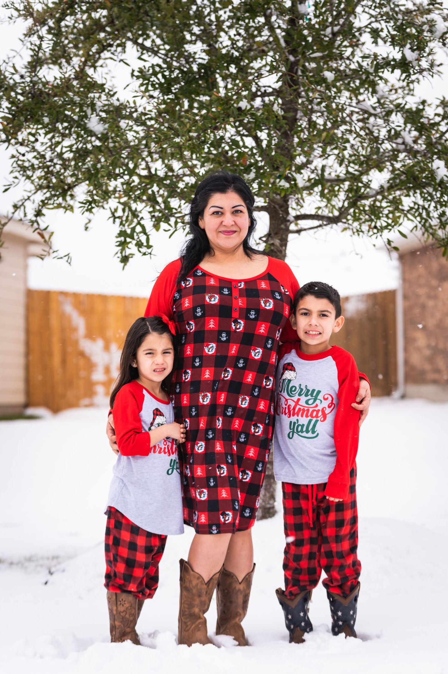 Family wearing coordinated red and plaid outfits poses together in the snow.